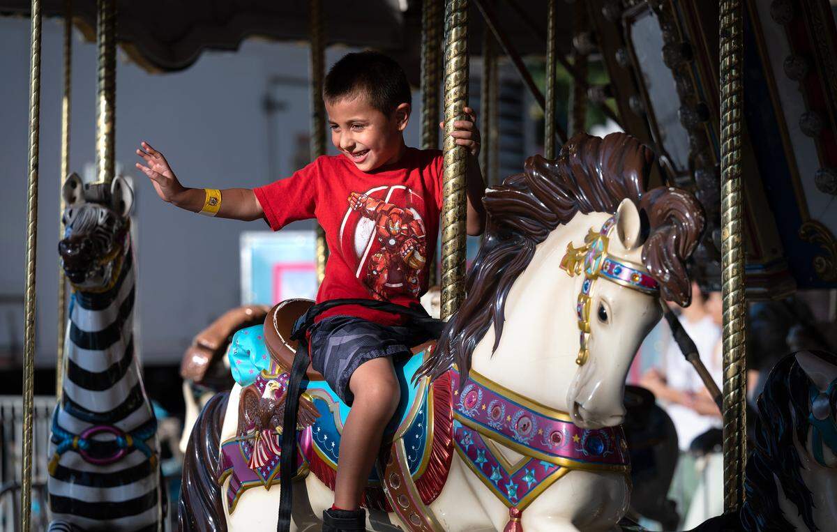 Jeremy Lopez Jr. waves to his father from the carousel in the midway at the Stanislaus County Fair in Turlock, Calif., on Thursday, July 14, 2022.