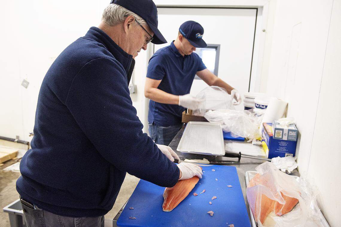 Ohana Seafood owner John Mensonides, left, slices salmon at his shop on 7th Street in Modesto, Calif., on Friday, March 27, 2020.