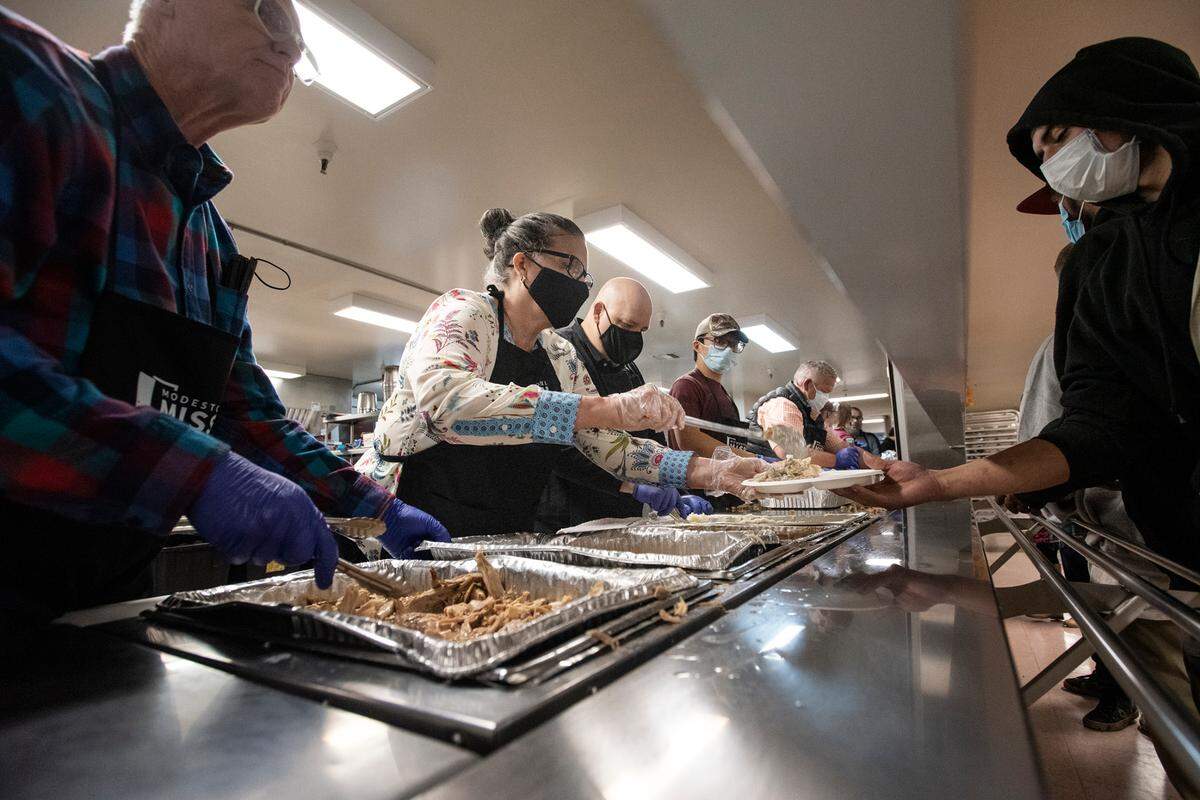 Modesto Mayor Sue Zwhalen, middle, and councilmember David Wright, left, serve a Holliday meal during the Great Thanksgiving Banquet & Bundle-Up at the Modesto Gospel Mission in Modesto, Calif., on Wednesday, Nov. 24, 2021.
