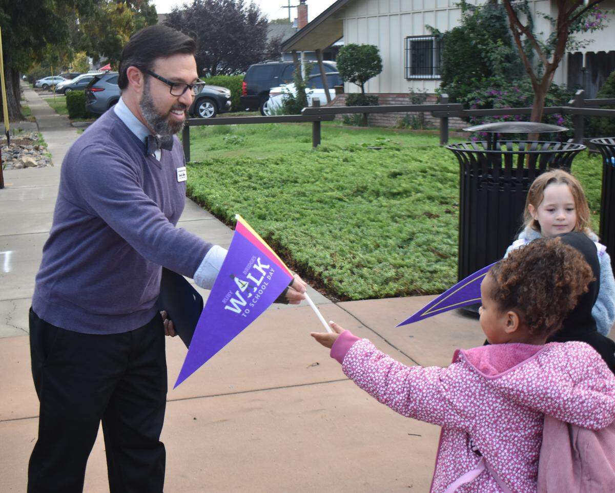 Students at Woodrow Elementary celebrated Ruby Bridges Walk to School Day on Friday, Nov. 14, 2025, by walking a short distance on the Virginia Corridor Trail from Rumble Road to their school. Here, David Collins, Love Our Schools program director with Love Stanislaus County, gives a pennant to kindergartner Aya Mori.