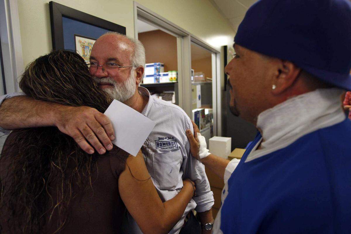 Father Gregory Boyle, center, hugs Nancy Delgadillo while David Minjarez looks on at Homeboy Industries’ headquarters in Los Angeles, California, on September 14, 2010. Minjarez’s neck is bandaged after having a tattoo removed at Homeboy Industries.
