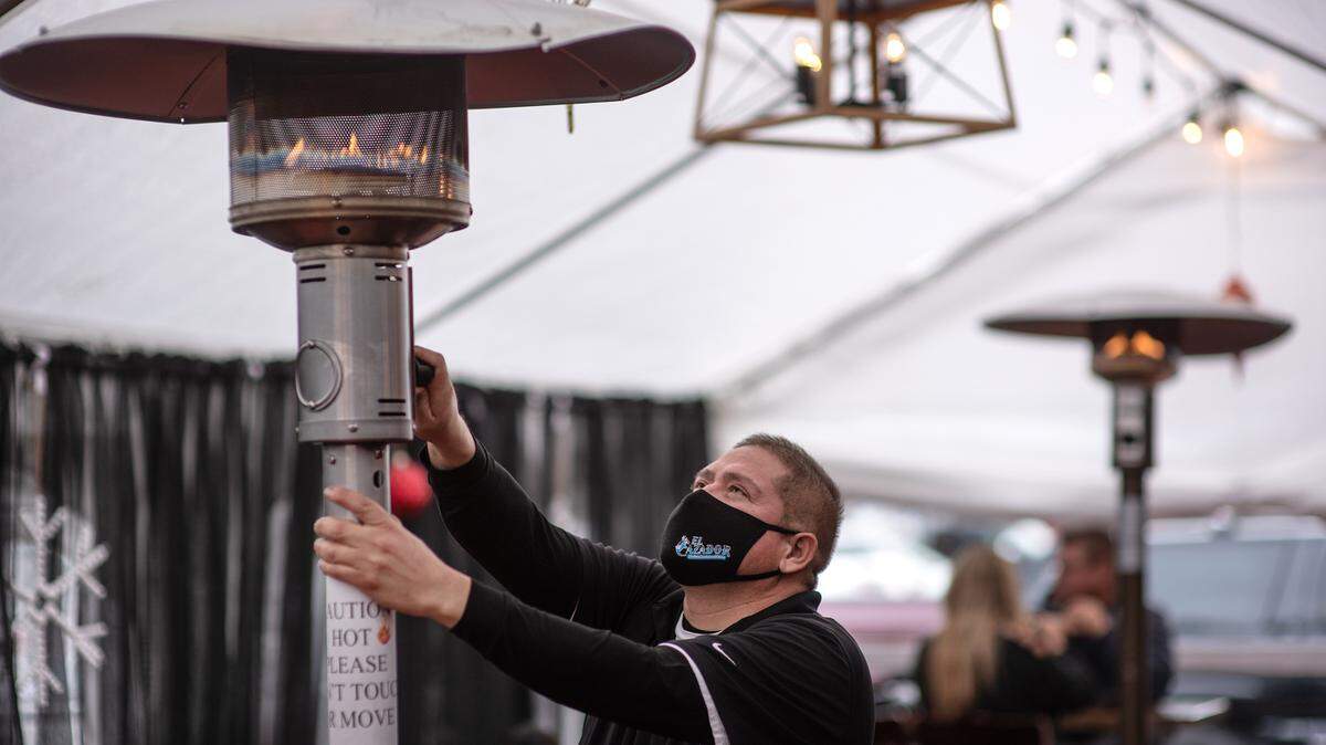 Christian Mejia ignites an outdoor heater at customers eat outside at El Cazador Mexican Restaurant in Modesto, Calif., on Tuesday, Nov. 17, 2020.