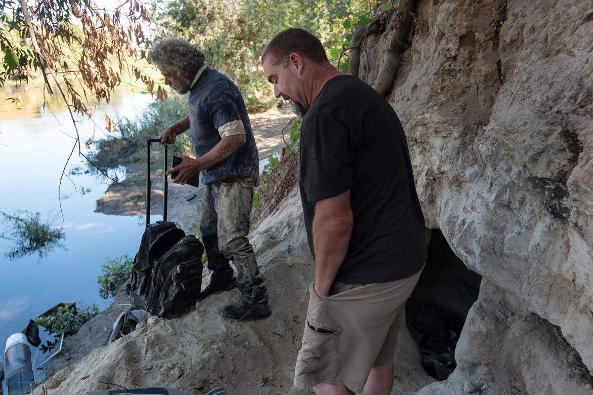 A man exits a hand dug cave as Chris Guptill, right, shows how homeless people have been digging into the river embankment along the south side of the Tuolumne River near Crater Avenue in west Modesto, Calif., Thursday, Oct. 27, 2022.