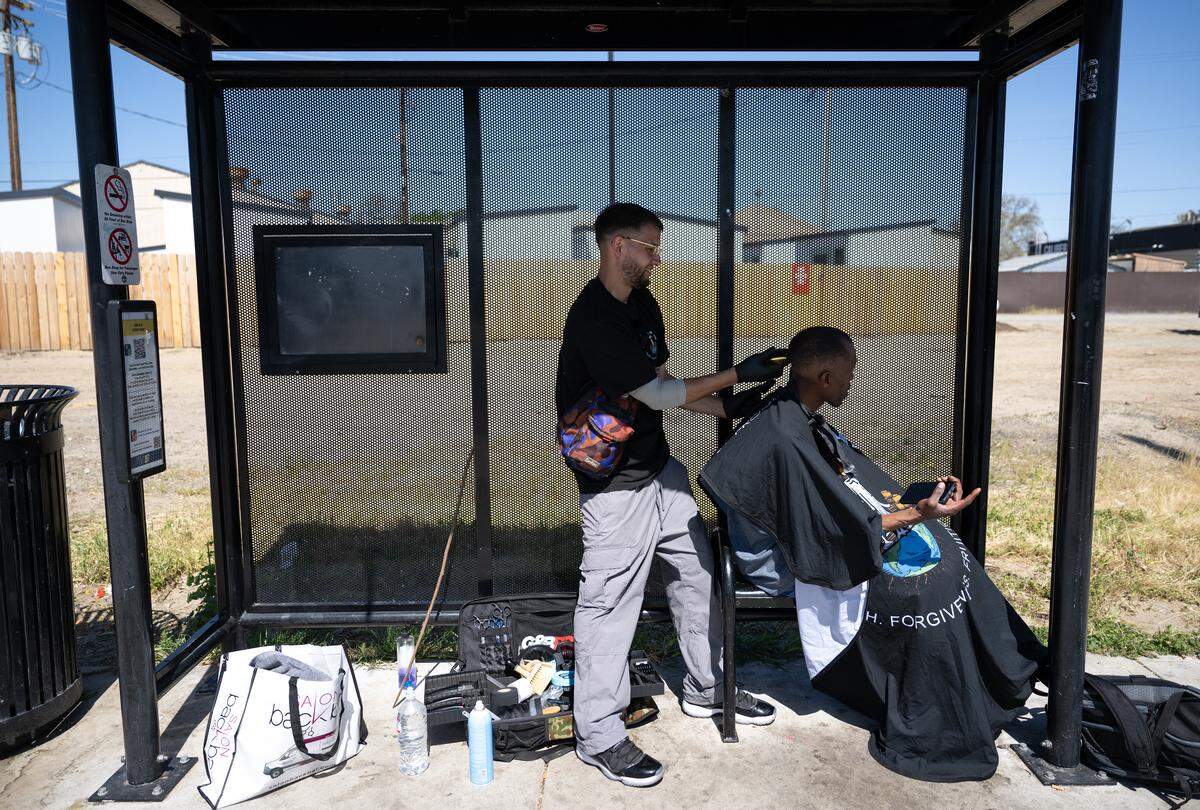Paul Samsin, aka Sammy, cuts the hair of Johnny Ray at a bus stop on Ninth Street in Modesto, Tuesday, April 8, 2025.
