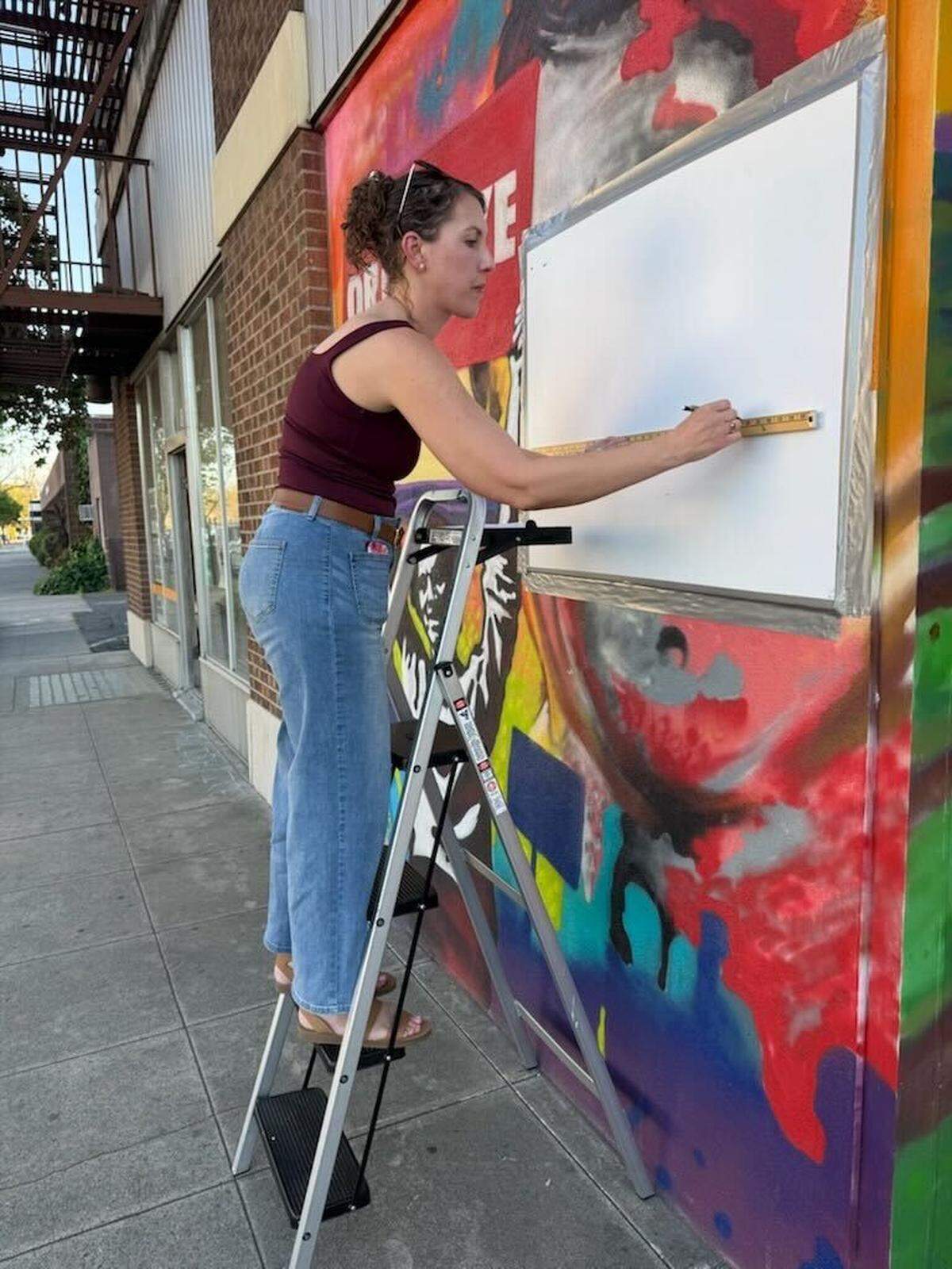 Modesto Peace/Life Center board member Megan Paravanno works on a sign covering Cesar Chavez’s face on a mural at the downtown center on March 18, 2026.