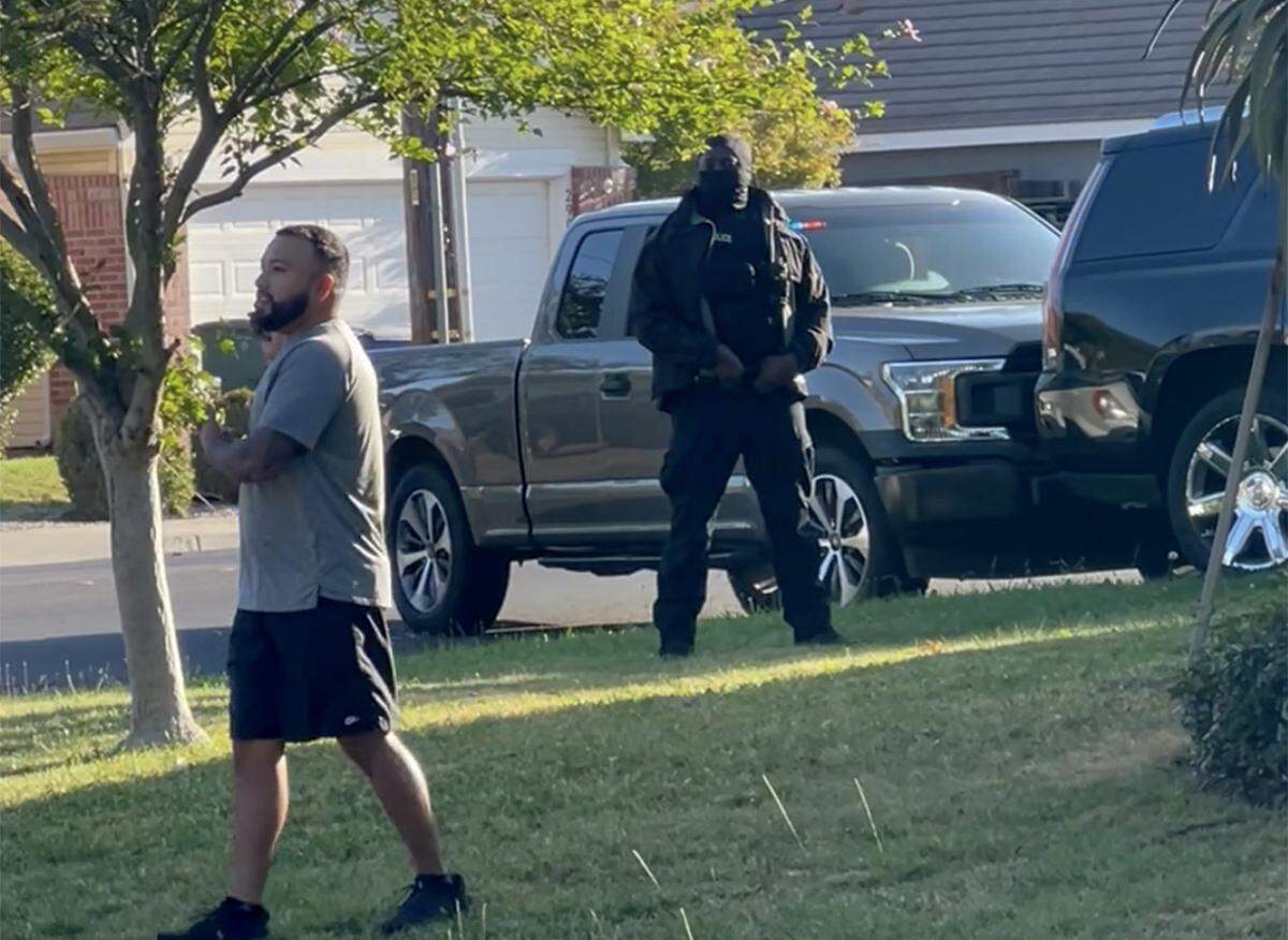 In a screen capture from video, a man speaks to an off-camera woman who was filming armed agents outside of Modesto home on Sept. 11. At right is a masked agent.