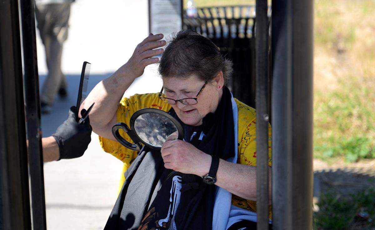 Katherine Root checks her haircut she received from street barber Paul Samsin at a bus stop on Ninth Street in Modesto, Tuesday, April 8, 2025.