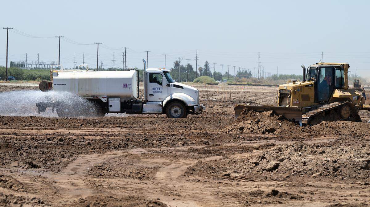 Una camión cisterna humedece el suelo mientras los trabajadores preparan el sitio del nuevo Costco en Riverbank, California, el miércoles 9 de agosto de 2023.