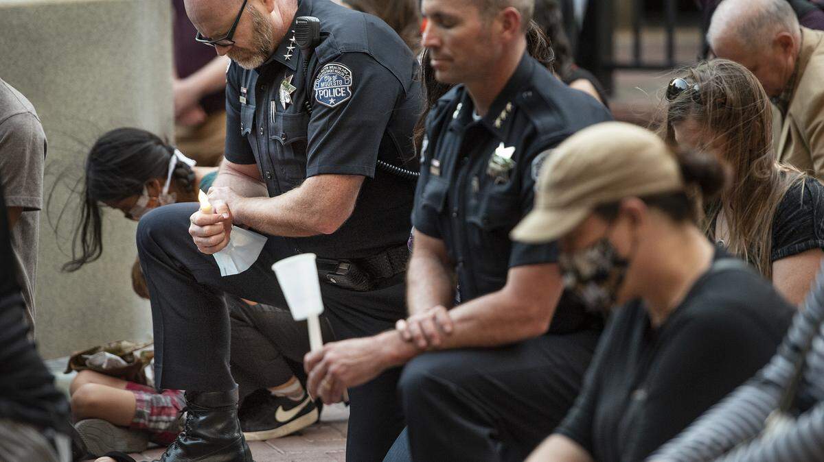 Modesto Police chief Galen Carroll, left, kneels on the brick pavement with other attendees for 8 minutes and 46 seconds in an extended moment of silence during a candlelight vigil for George Floyd at 10th Street Place in Modesto, Calif., on Friday, June 5, 2020. 8 minutes and 46 seconds is the time that prosecutors say Floyd was pinned to the ground by a Minneapolis police officer before he died last week in Minnesota.