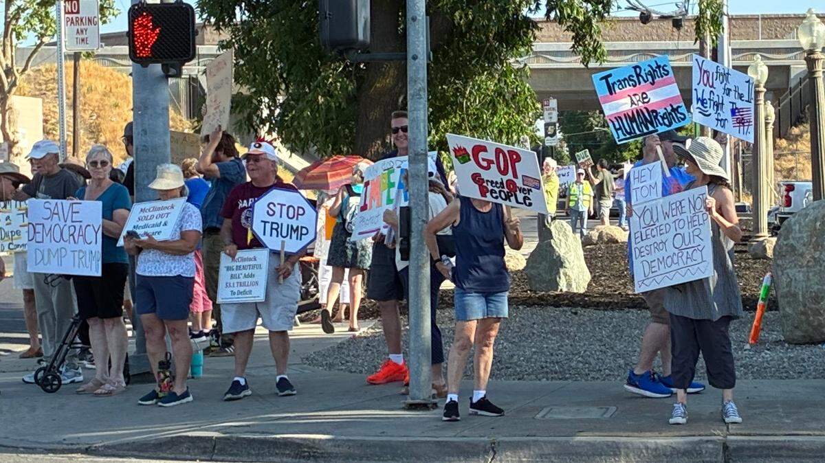 Dozens of people gather around the corner holding signs that read "Stop Trump" and "Trans Rights are Human Rights"