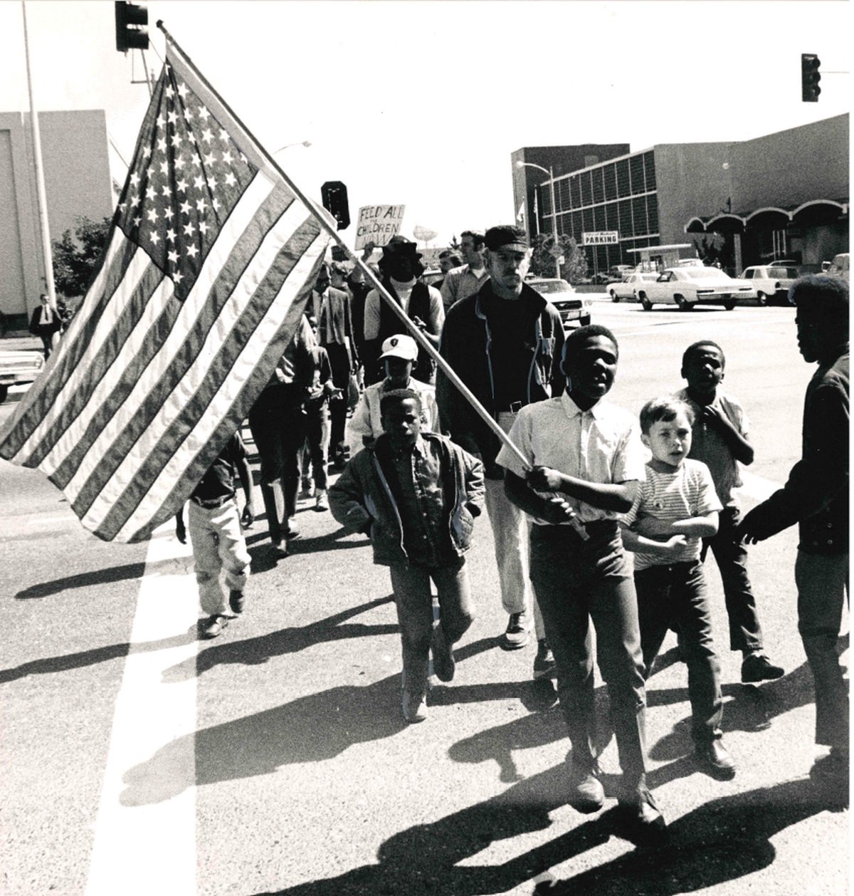A child holds up a large flag marching through downtown Modesto with other children following behind.