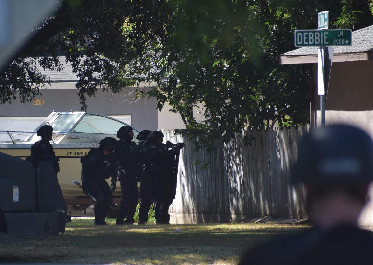 Police officers prepare to tear down fence boards at a home following a fatal shooting on Debbie Lane in central Modesto on Sunday afternoon, July 10, 2022.