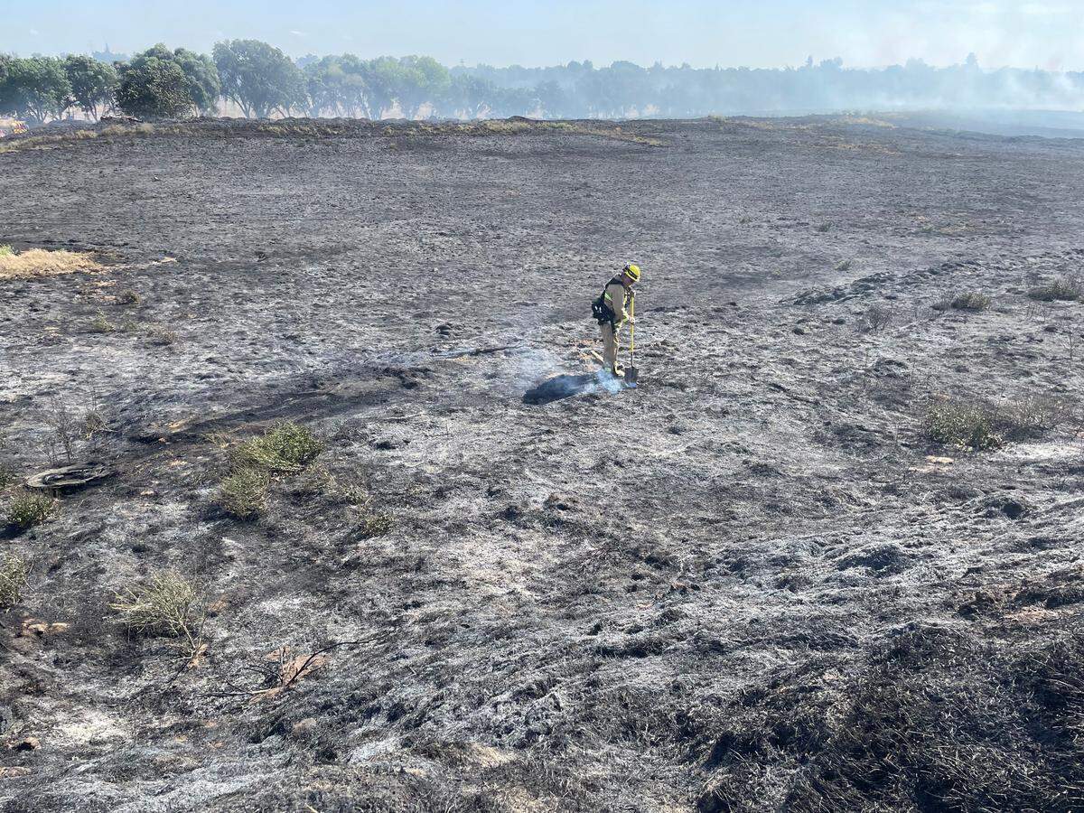 A firefighter extinguishes hot spots at a vegetation fire near Modesto’s airport neighborhood on Monday afternoon, May 2, 2022.