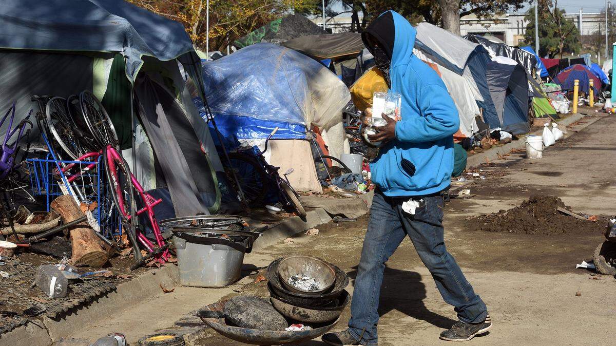 A homeless man bundled up against the cold carries food to his campsite on Monday morning December 3, 2018 at Beard Brook Park in Modesto, Calif.
