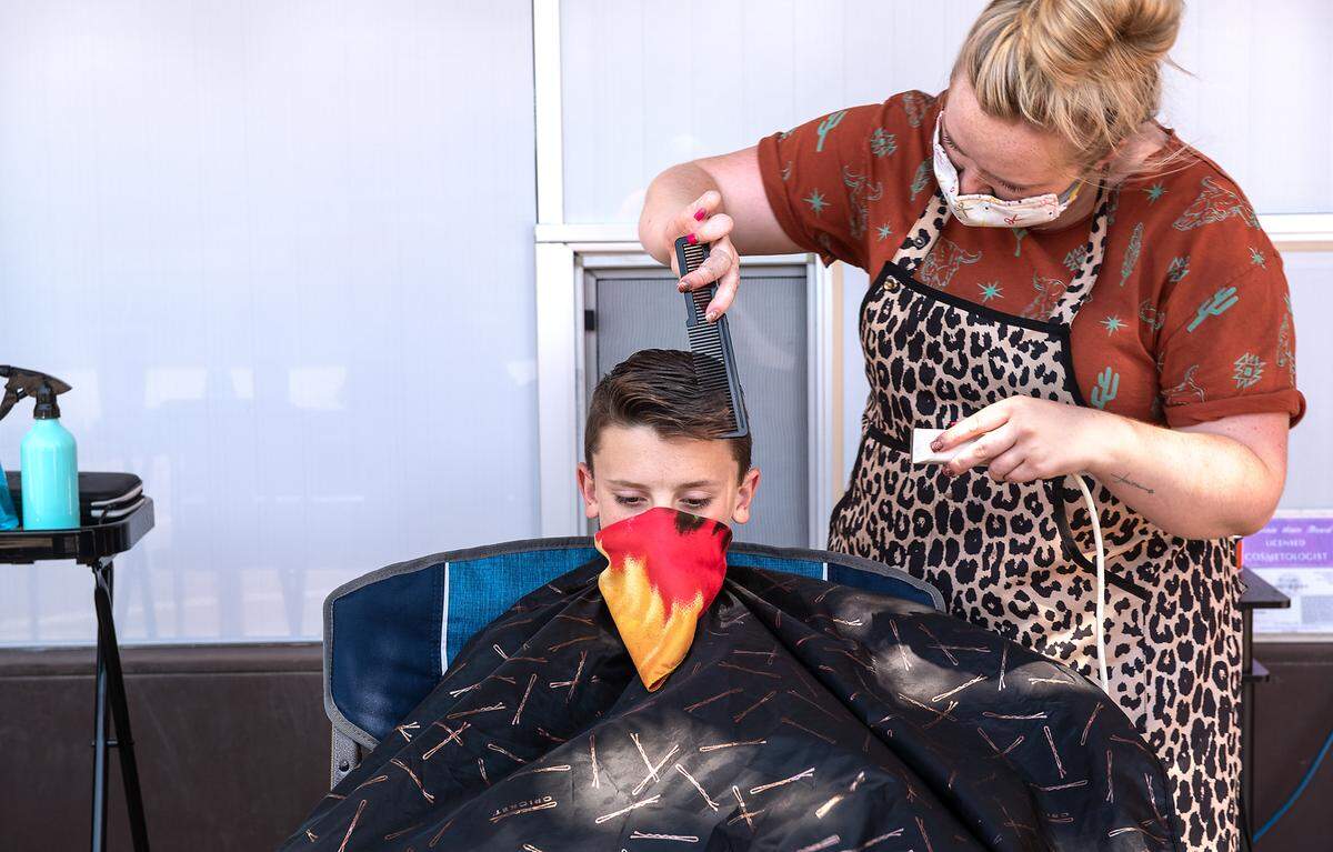 Stylist Kaitlyn Coker gives Carter NeVille, 13, a haircut on the sidewalk outside Revive Salon in Oakdale, Calif., on Saturday, August 1, 2020.