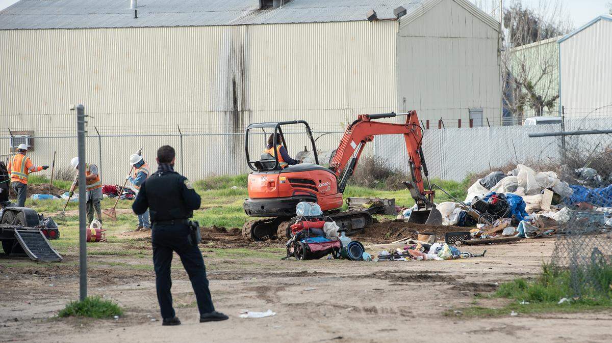 Turlock police watch contractors clear a homeless encampment between off West Main Street in Turlock, Calif., on Thursday, March 18, 2021.