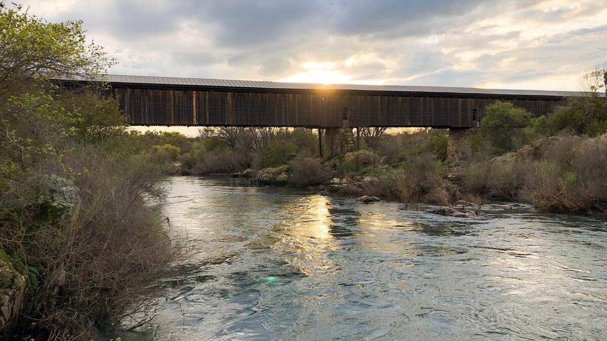 The sun sets behind the Knights Ferry covered bridge at the Stanislaus River on March 20, 2019.