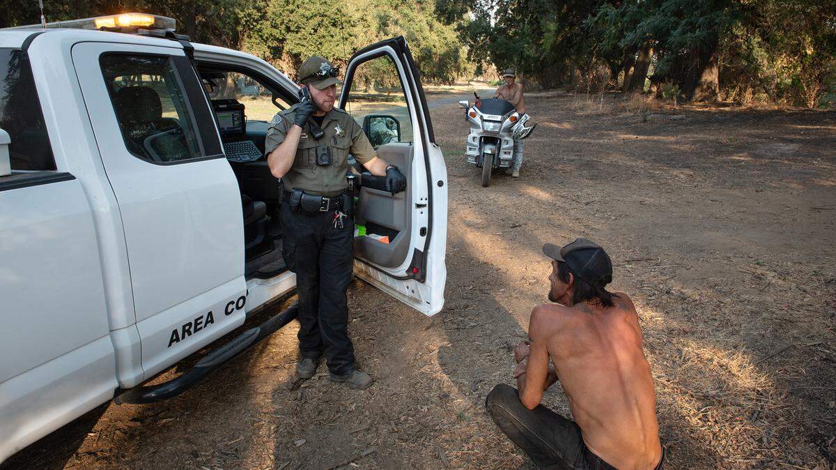 Modesto park ranger Justin Rocha, right, informs Alan Sanchez of a new court date on a previous citation for illegal camping. Photographed in Tuolumne Regional Park in Modesto, Calif., on Friday, September 9, 2022.