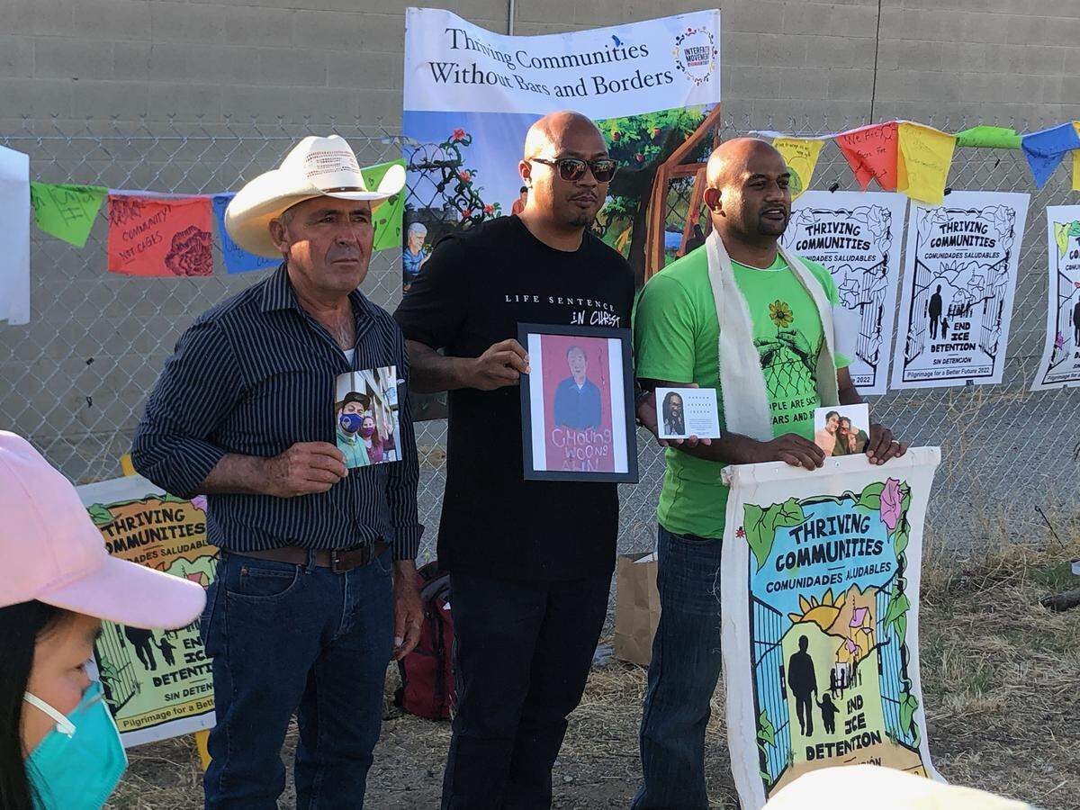 Former inmates Sithy Bin, center, and Michael Prasad, right — both of Modesto — hold images of detainees who have died in custody. They are shown May 29, 2022 at the Pilgrimage for a Better Future, an interfaith tour of ICE detention centers, outside the Mesa Verde ICE Processing Center in Bakersfield. Prasad is not related to Salesh Prasad, a former inmate from Modesto who faces deportation.