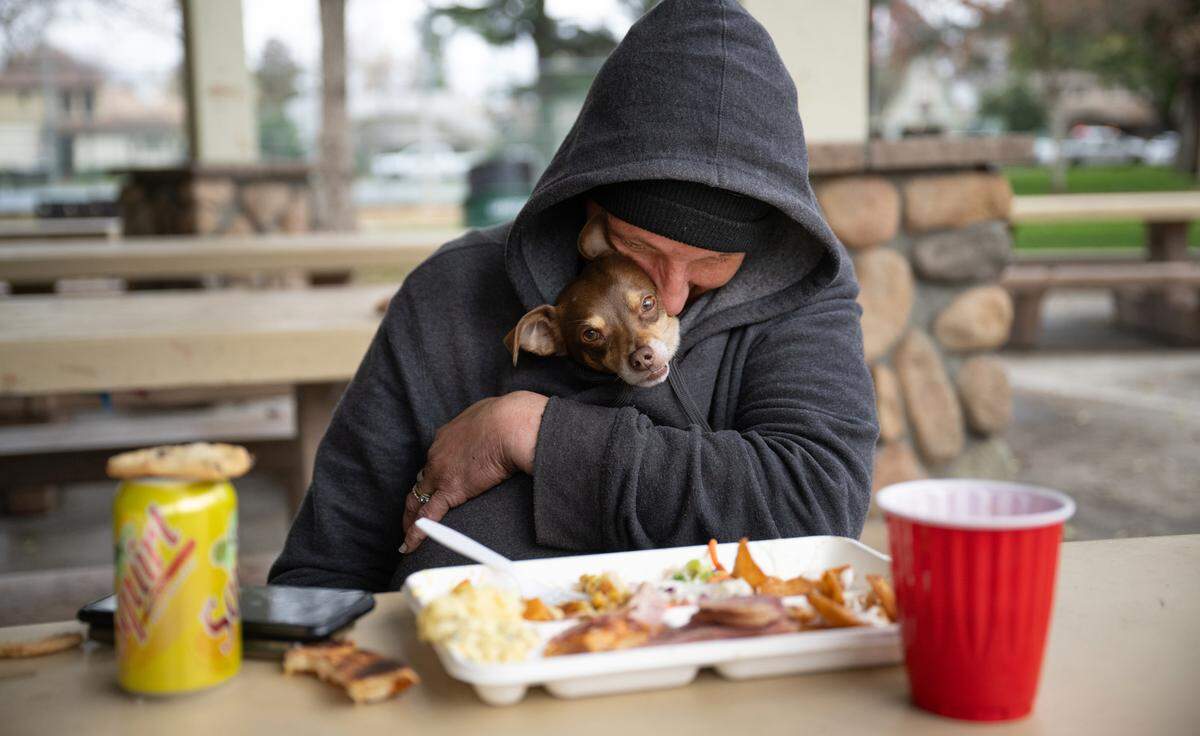 Tiffany Qualls and her dog Baby Jay eat lunch during a celebration-of-life picnic for Carl Wolden at Graceada Park in Modesto on Friday, Dec. 13, 2024.