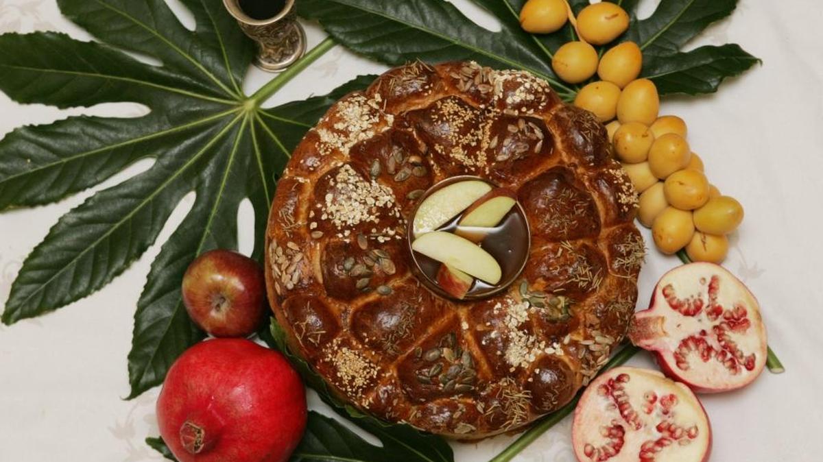 A selection of symbolic foods that have a place in the classic Rosh Hashana meal includes a round loaf of challah bread, center, topped with apples dipped in honey.