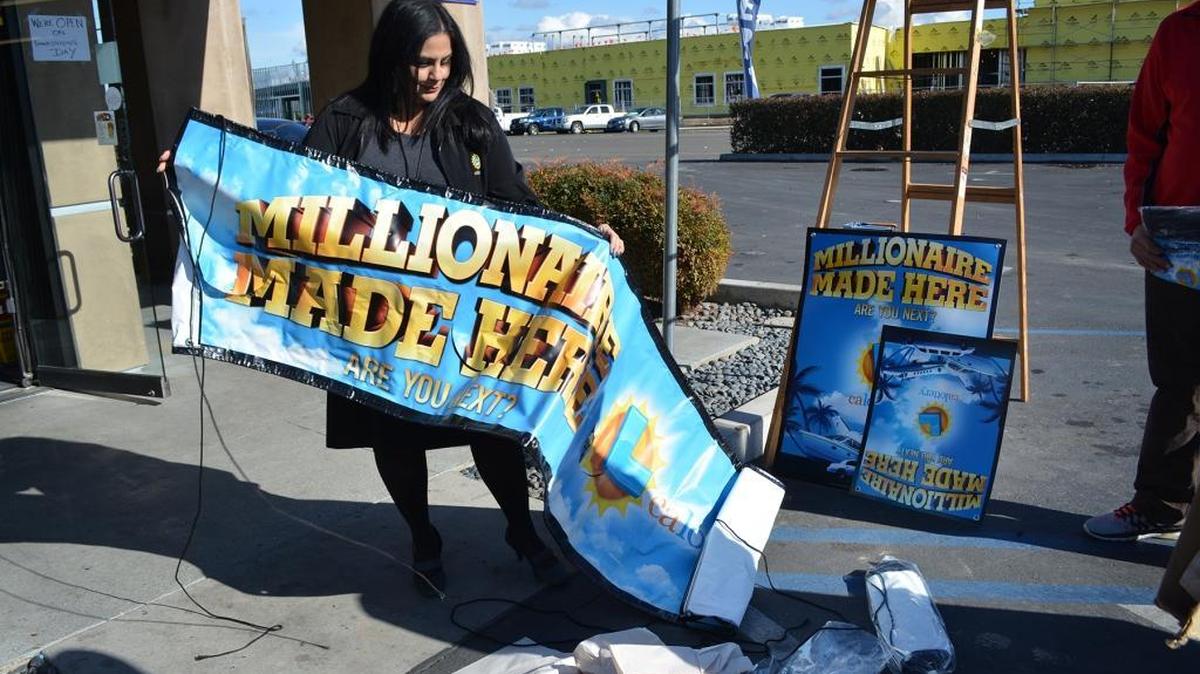 Paulina Ishaya, California Lottery sales representative based in Modesto, unveils a “Millionaire Made Here” banner along with signs, stickers and T-shirts for Fast Mart on Coffee Road, where a $10 million winner was announced Wednesday, Nov. 25, 2015.