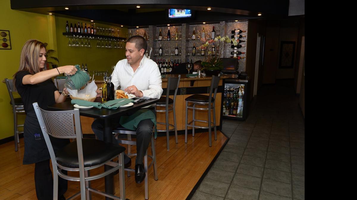
Server Maria Baires refills water for customer Jose Zamora on Thursday at Famiglia Bistro.
