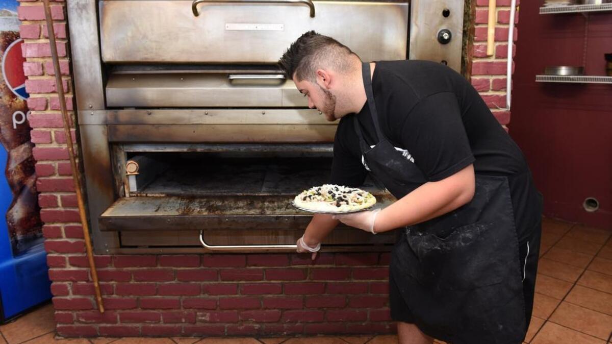Basam Jajo puts a pizza into the brick oven at Luigi’s Pizza on July 1, 2015.