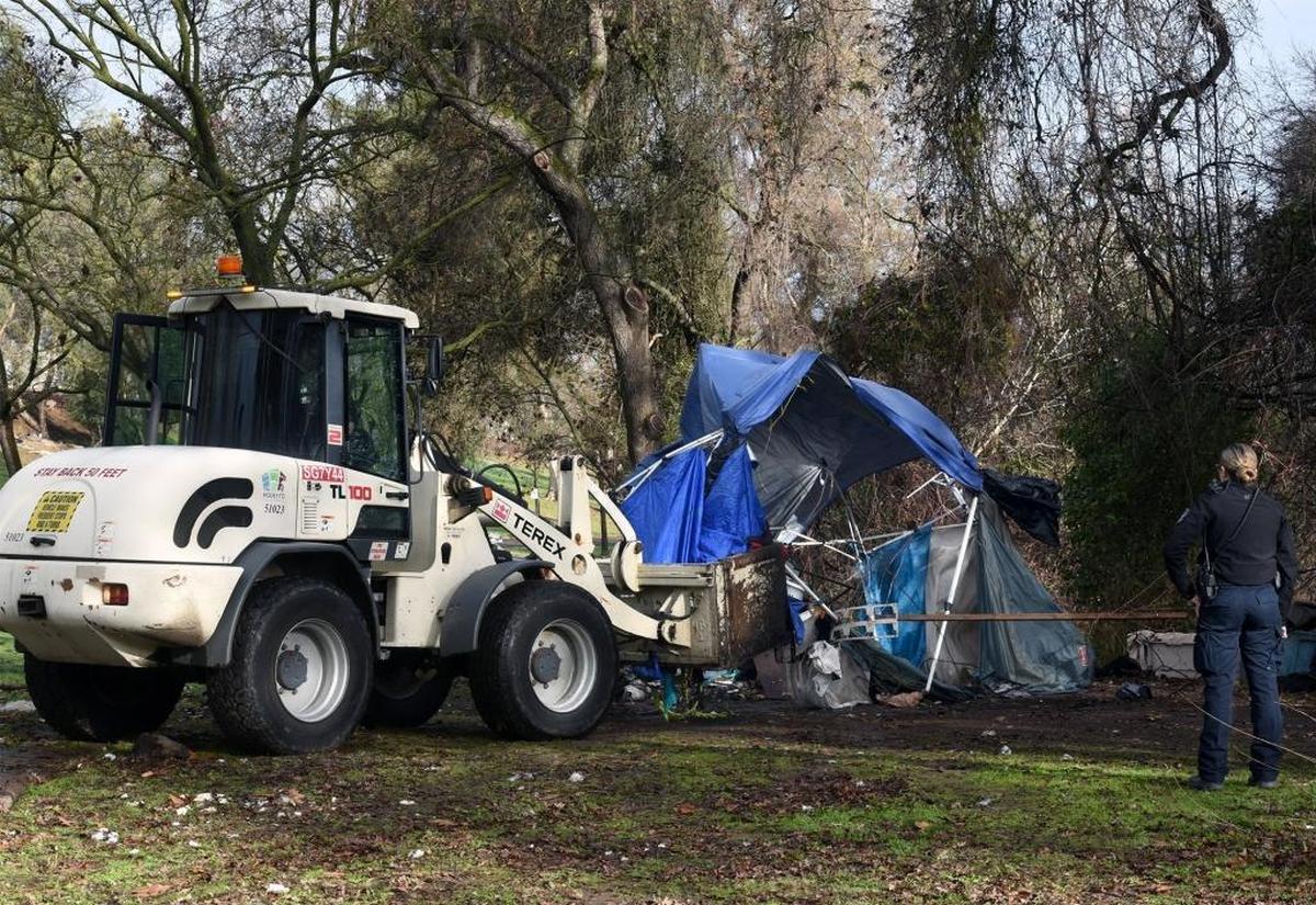 A Modesto police community service officer stands by as City of Modesto park crews cleanup a campsite where homeless people were living Thursday morning January 25, 2018 in Beard Brook Park in Modesto, Calif.