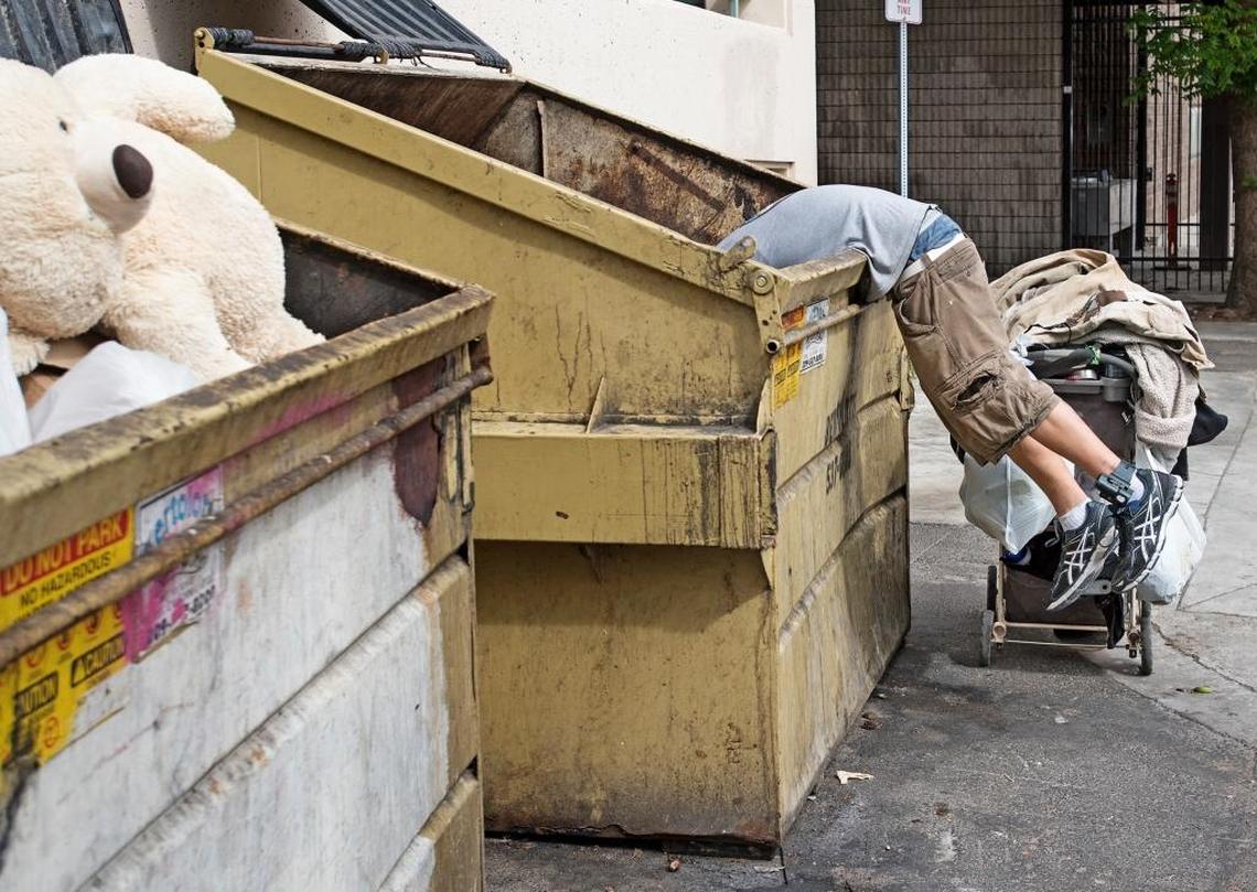 A homeless man digs through a Dumpster in downtown Modesto, Calif., on Wednesday, May 16, 2017.