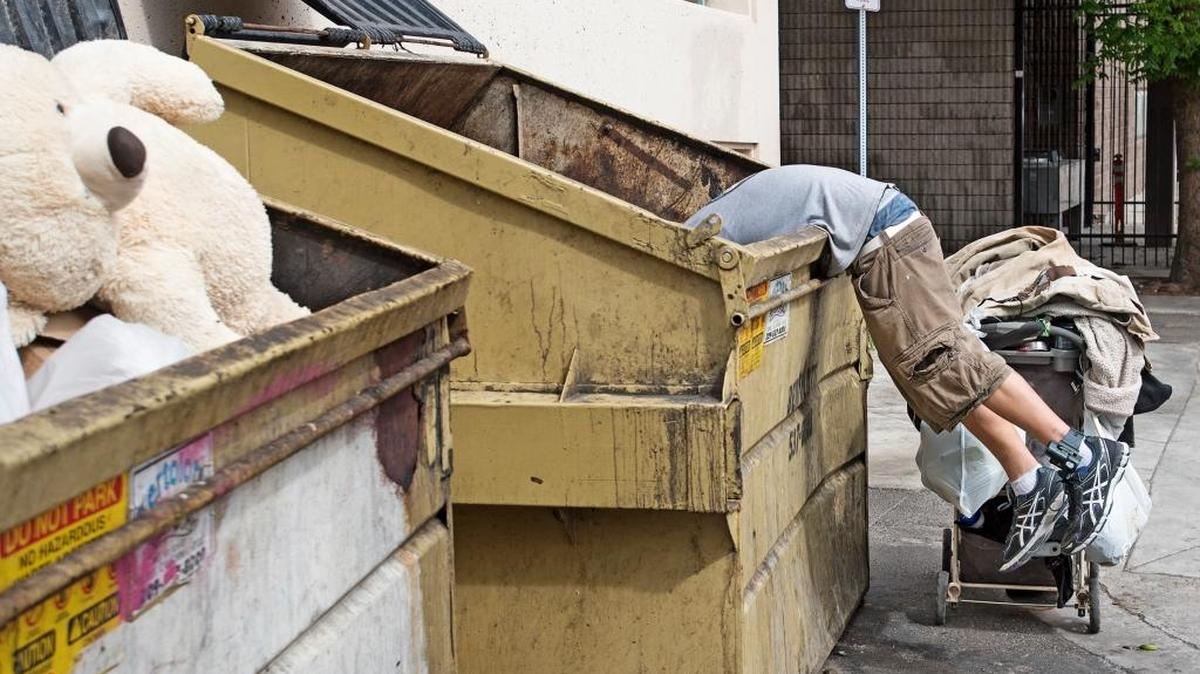 A homeless man digs through a Dumpster in downtown Modesto, Calif., on Wednesday, May 16, 2017.