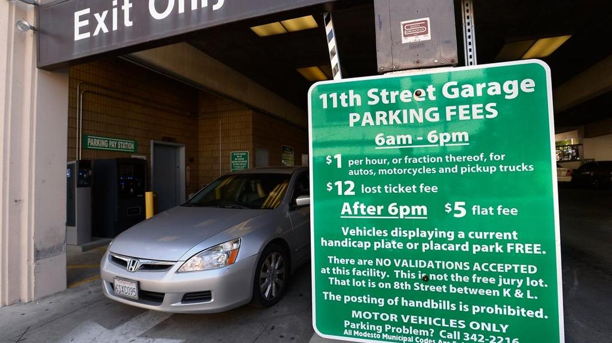 A car exits the city of Modesto parking garage on 11th Street between J and I streets near a sign displaying parking fees.