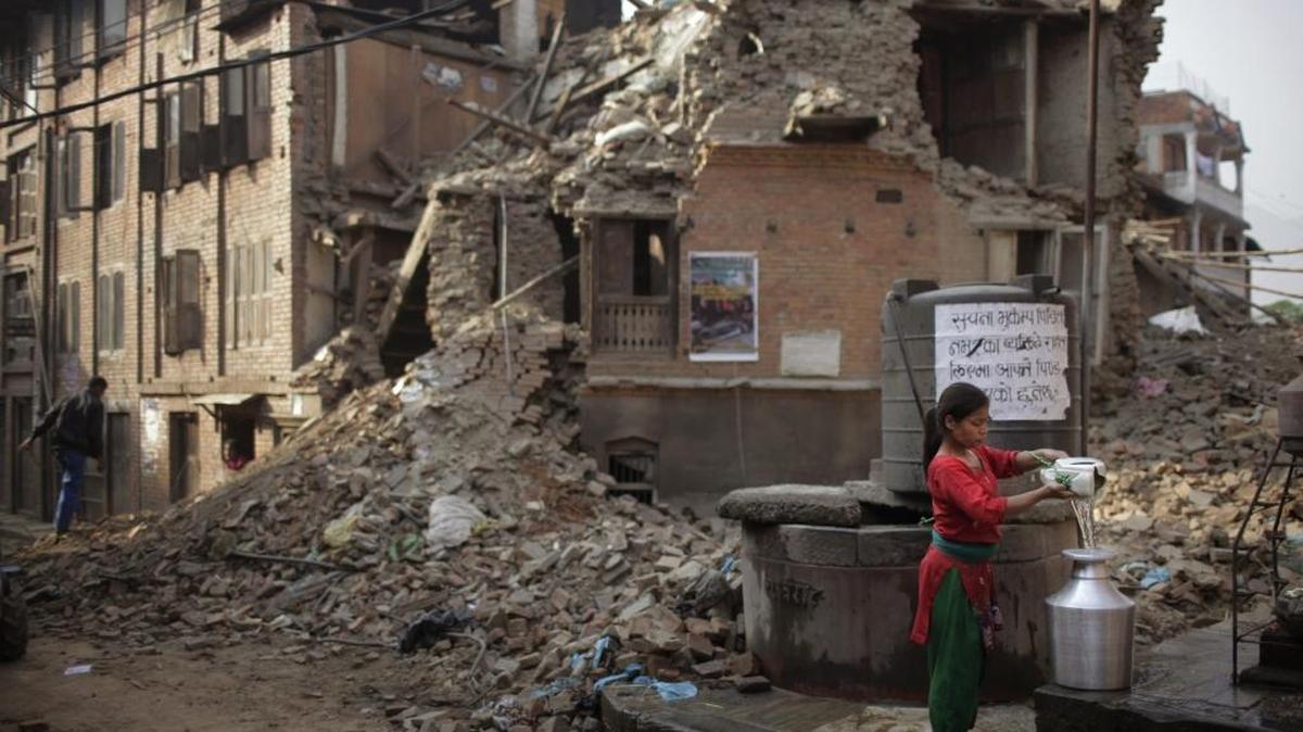 A Nepalese woman fills a jug with drinking water from a well in late May in front of damaged houses one month after the deadly 7.8 magnitude earthquake in Kathmandu in 2015.