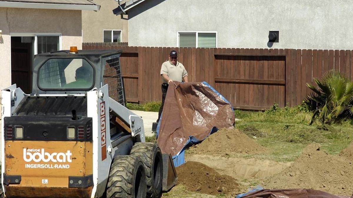 Ceres police Sgt. Patrick Sullivan holds a tarp as a bobcat replaces dirt from a hole dug by authorities in the backyard of an Alexis Court home in Ceres. Alycia Mesiti’s remains were found buried in the backyard in March 25, 2009