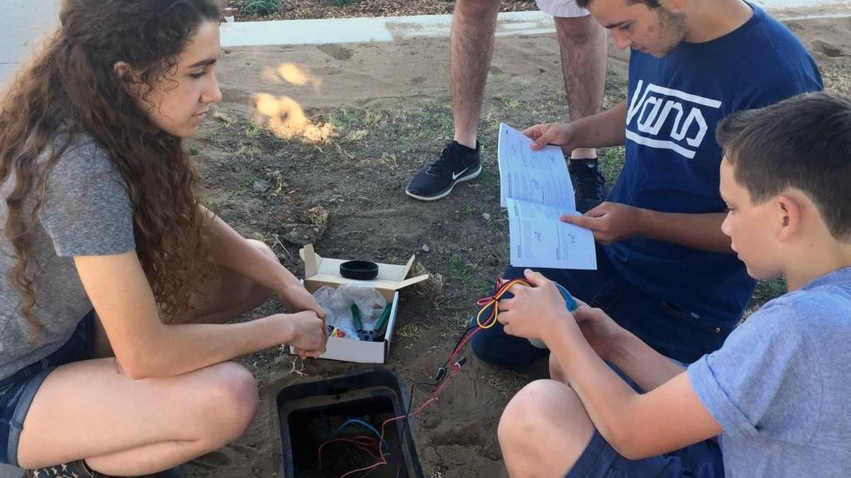 FFA students Kyle Damos, reading directions, Faith Haile and brother Lane Haile work on putting a timer on the new drip irrigation system being put in place in front of Downey High in Modesto, Calif., on Thursday, June 2, 2016.