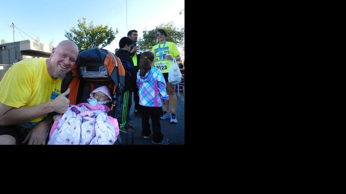 
Charlie Brown, 46, of Modesto gives a thumbs-up with his sleeping granddaughter, 9-month-old Bay Sousa. Brown ran the 5-kilometer race on Sunday in the Modesto Marathon. He ran the race while pushing his granddaughter in her stroller. 
