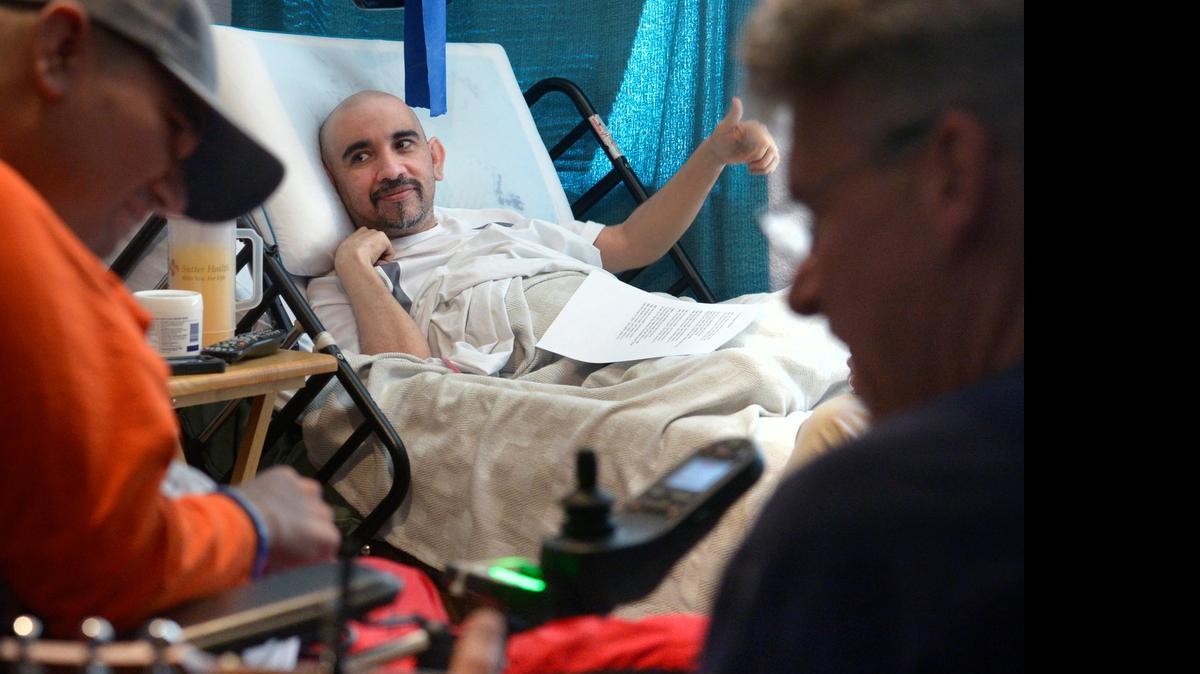 
Miguel Perez gives a thumbs up while listening to live music with brother Juan, sitting at left in the wheelchair, as guitarist singer Don Lawson plays at right.
