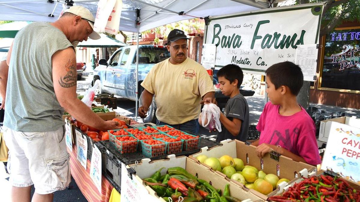 
Tony Fields and sons Speedy and Arthur, right, help a customer pick produce Saturday at the Turlock Certified Farmers Market.
