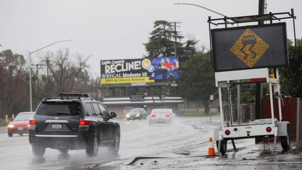 A caution sign urging drivers to slow down around a sharp turn on the wet road sits along the side of Scenic Driver east of Bodem Street on Sunday. Many accidents happen just east of the intersection because of speed and wet roads according to Modesto Police. Rain blanketed the Central Valley Sunday resulting in puddles and flooding of some roads Jan. 8, 2017.