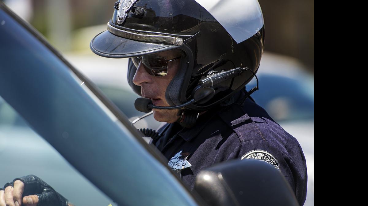 
Modesto police Officer Jeff Hopkins, wearing a body camera on his motorcycle helmet, writes a speeding citation on Ninth Street in Modesto last month. 

