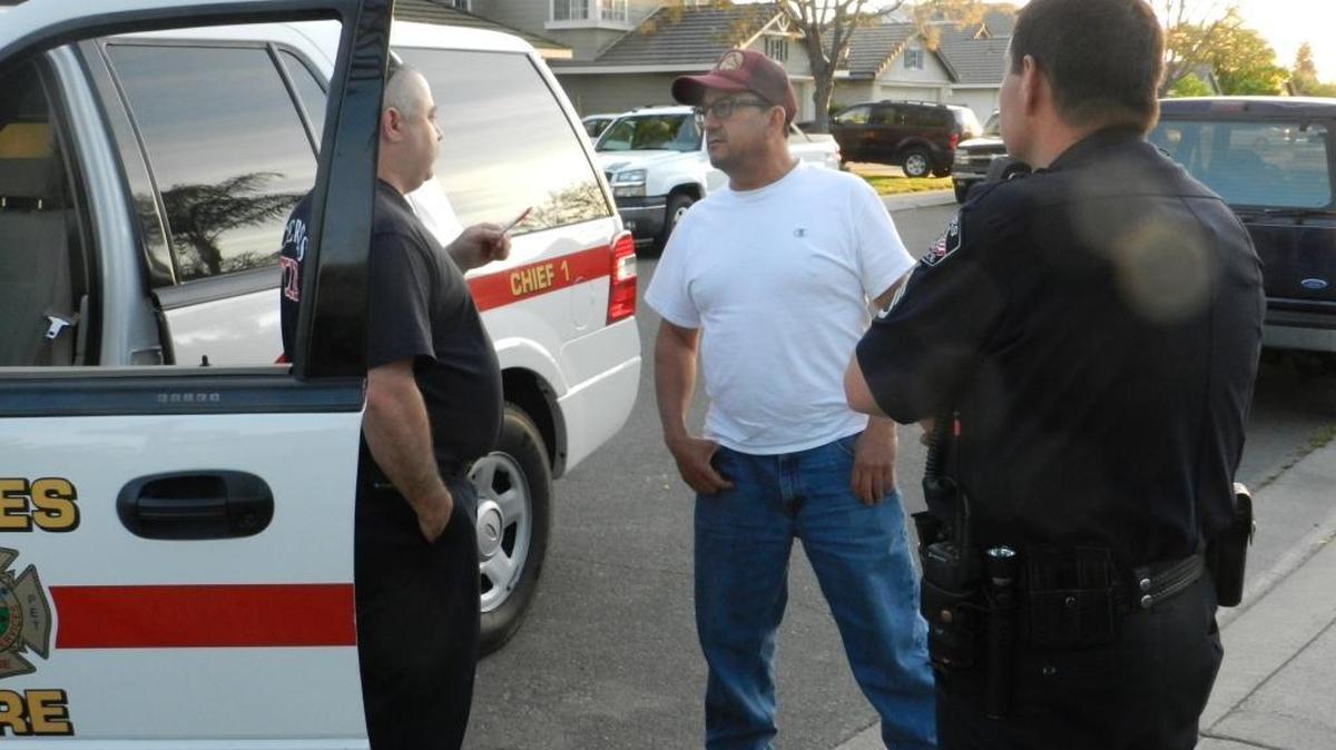 An unidentified beekeeper (center) talks with Ceres police and fire personnel outside one of two homes where swarming bees injured two people and killed a dog Sunday, April 2, 2017.