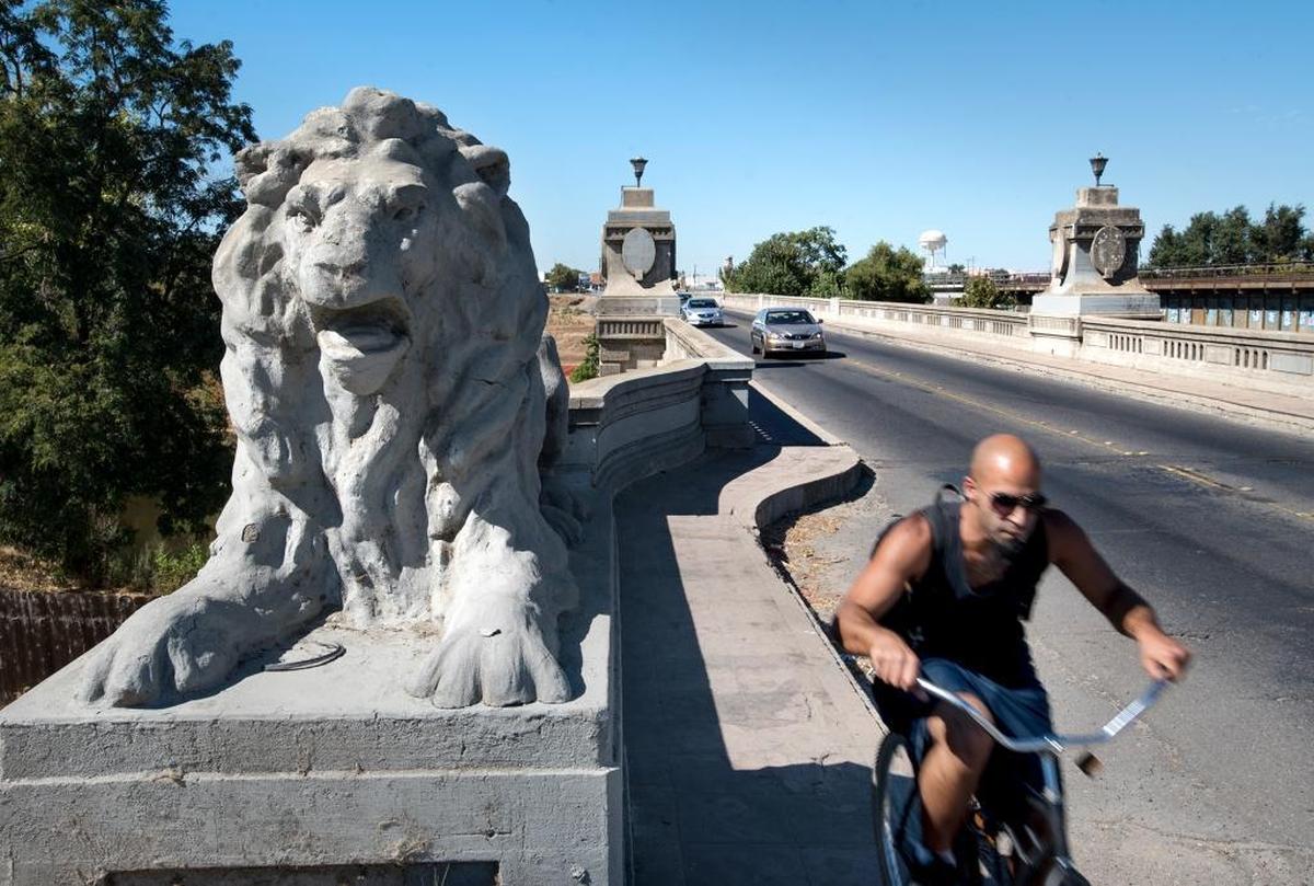A bicyclist passes one of the four lion statues on the Seventh Street Bridge in Modesto  in 2016. They will be preserved after the bridge is replaced, starting in January 2026.
