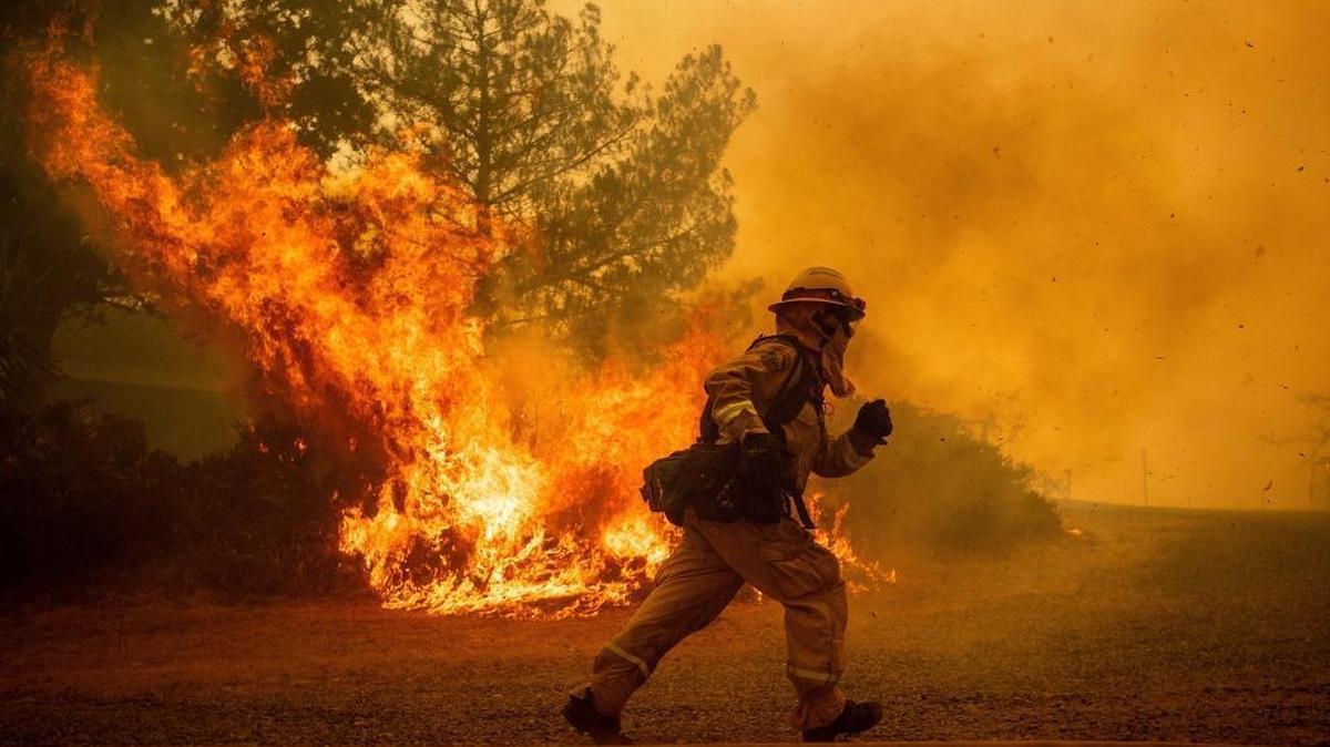 A firefighter runs while trying to save a home as a wildfire tears through Lakeport on July 31. The Mendocino Complex Fire has become California’s largest blaze in recorded history and triggered controversy over Verizon’s decision to “throttle” a fire agency’s communication’s data speeds.