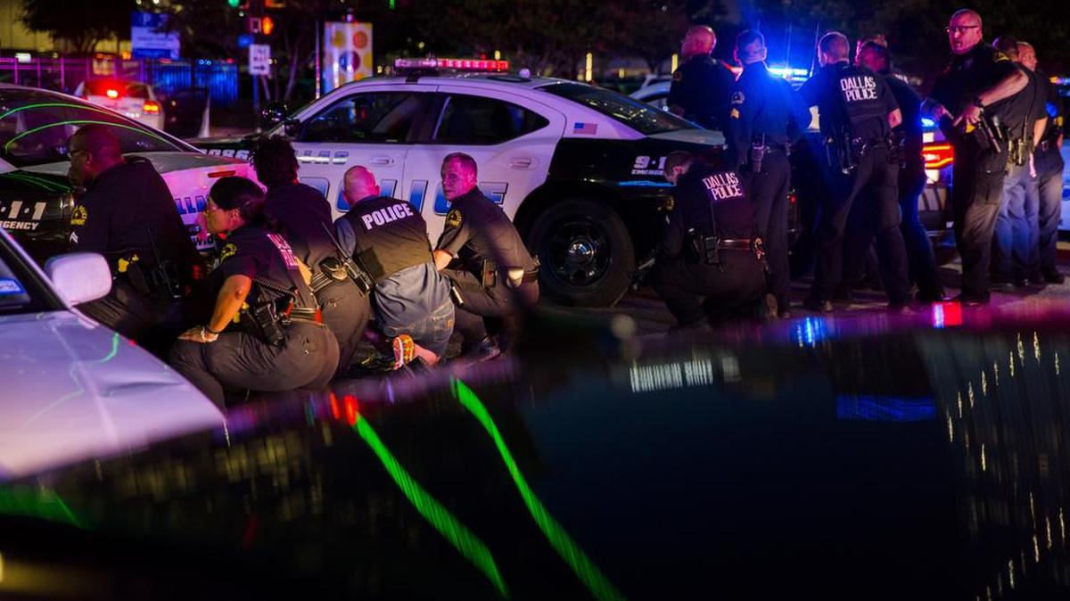 Dallas police officers crouch behind vehicles after shots were fired during a protest Thursday night. Five officers were killed and seven others wounded.