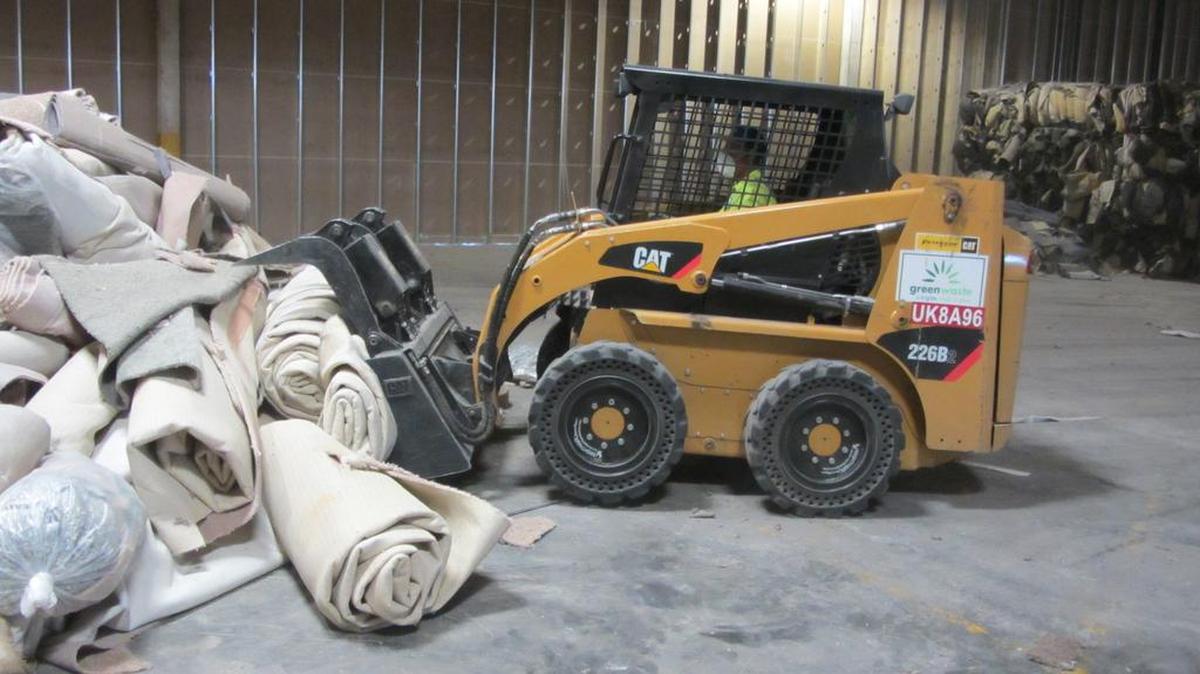 A small front-loader moves used carpet around a disposal facility. The carpet will not be burned.