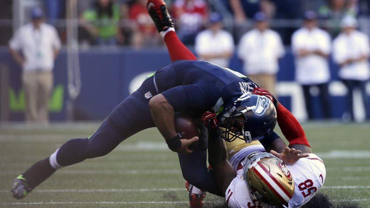 Seattle Seahawks quarterback Russell Wilson, top, is pulled down by San Francisco 49ers' Eli Harold in the second half of an NFL football game Sunday, Sept. 25, 2016, in Seattle.